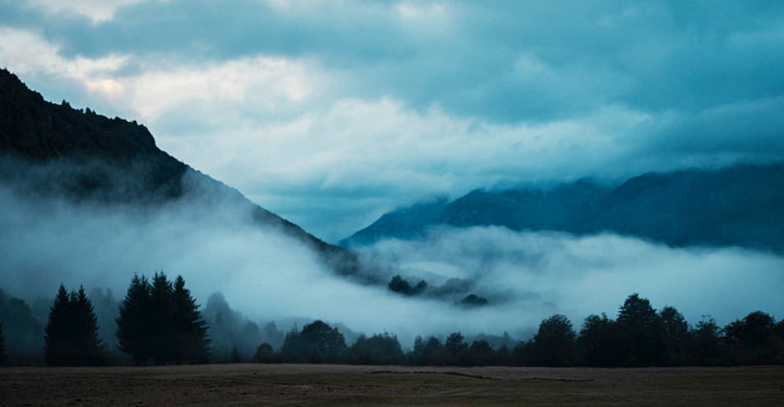 low lying clouds coat the mountains and enhance the silhouettes of trees at dusk in patagonia