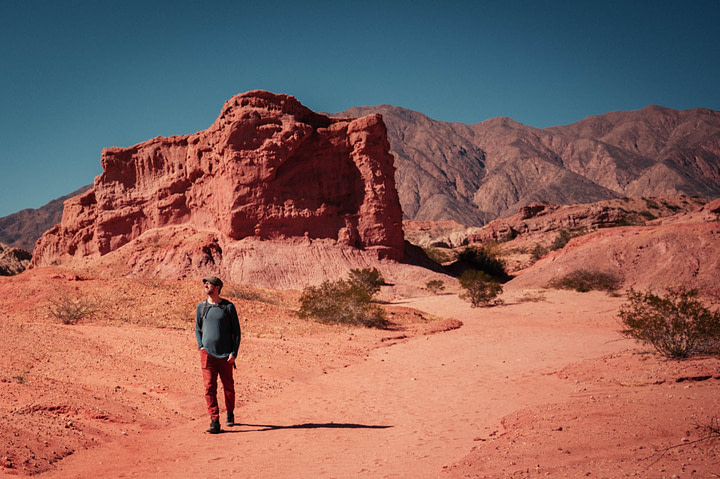 Theo wandering through a valley of pink sandstone rocks, with multicolored mountains in the distance. Quebrada de las Conchas, Cafayate Gorge, Salta Province - Argentina