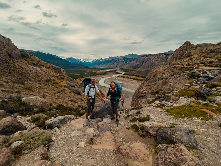 Maxine and Theo kitted out for a three day hiking trip standing against a backdrop of mountains and the Rio de las Las Vueltas valley in El Chaltén. Parque Nacional Los Glaciares (Glacier National Park), Argentina.